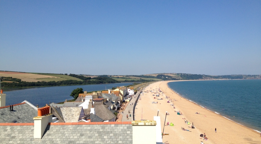 A view along Slapton Line from Torcross on a beautiful day in summer with blue sky and people playing on the beach at low tide
